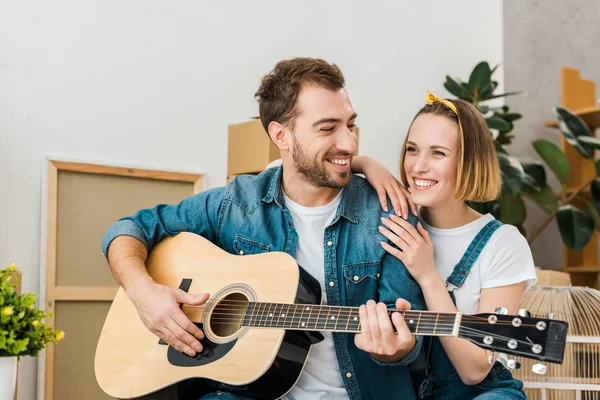 Усміхнений чоловік грає на акустичній гітарі дружині вдома — стокове фото