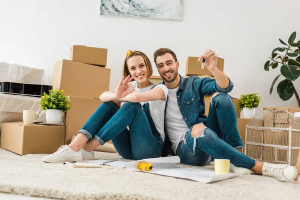 Sorrindo mulher mostrando bem sinal enquanto marido mostrando chaves — Fotografia de Stock