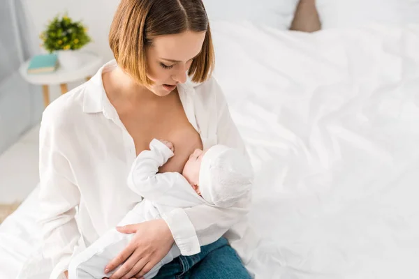 Overhead view of young mother in white shirt breastfeeding baby at home — Stock Photo