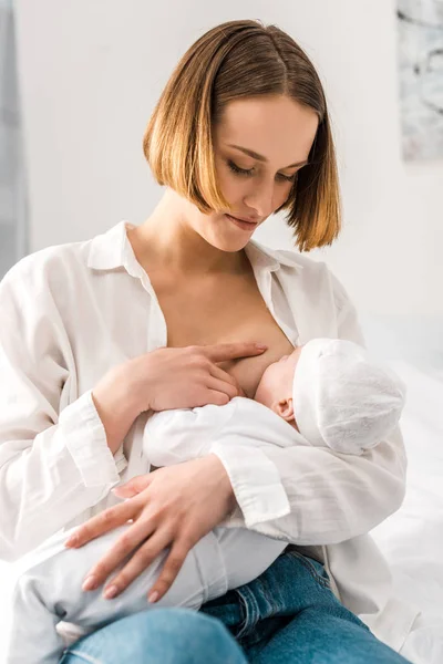 Young mother in white shirt breastfeeding baby at home — Stock Photo