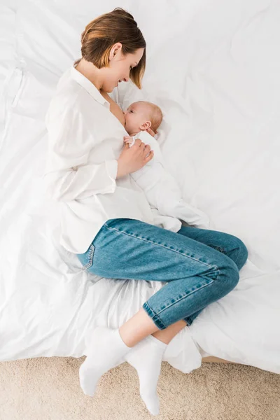 Top view of mother in white shirt lying on bed and breastfeeding baby — Stock Photo