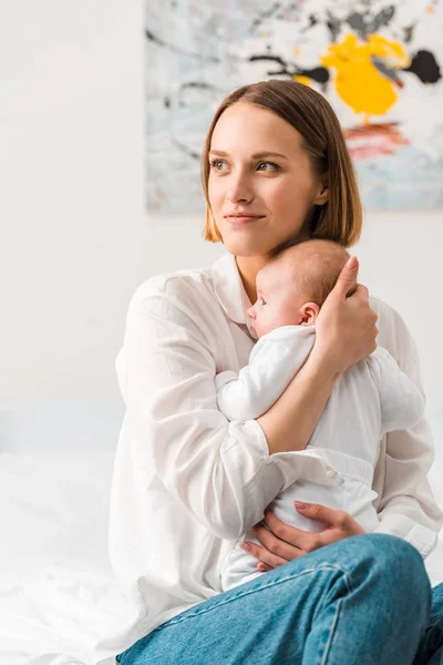 Glückliche Mutter im weißen Hemd, Baby in der Hand und zu Hause wegschauend — Stockfoto