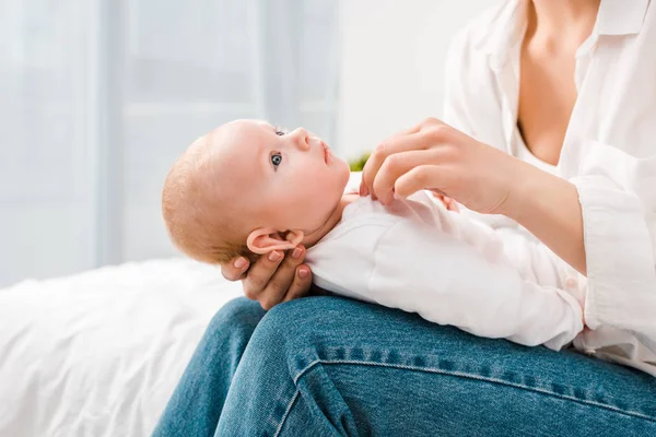 Cropped view of mother in white shirt holding baby at home — Stock Photo