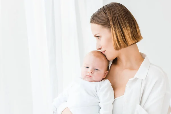 Jeune mère souriante en chemise blanche tenant bébé à la maison — Photo de stock