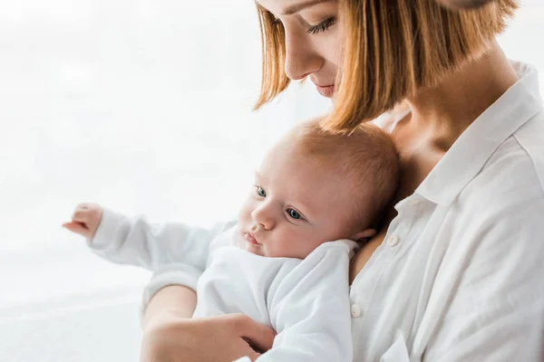 Young mother in white shirt holding baby at home — Stock Photo