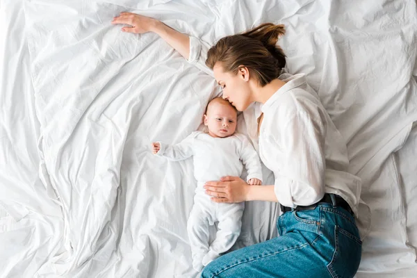 Вид зверху на матір в джинсах лежить на ліжку з дитиною — стокове фото