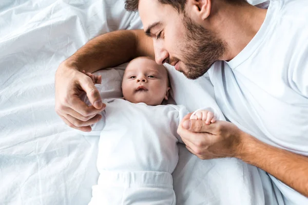 Happy bearded dad lying on white sheet with baby — Stock Photo