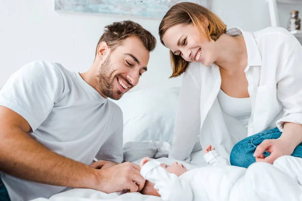 Jovens pais felizes olhando para o bebê na cama — Fotografia de Stock