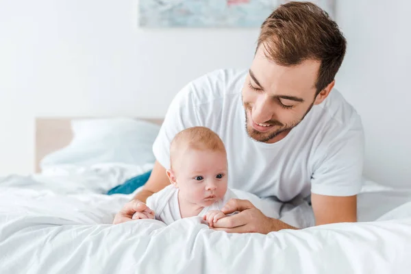 Smiling father lying on bed with baby in bedroom — Stock Photo