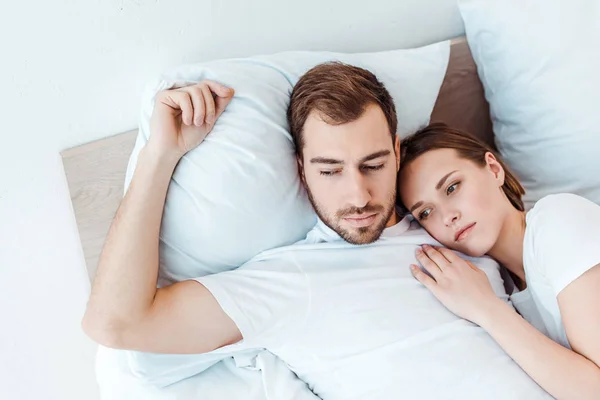 Pensive couple in white t-shirts lying on bed and looking away — Stock Photo