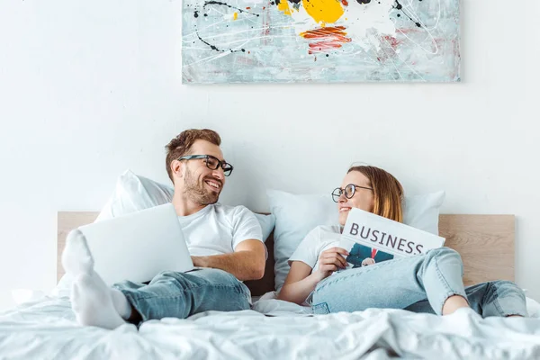 Couple in glasses with laptop and newspaper looking at each other — Stock Photo