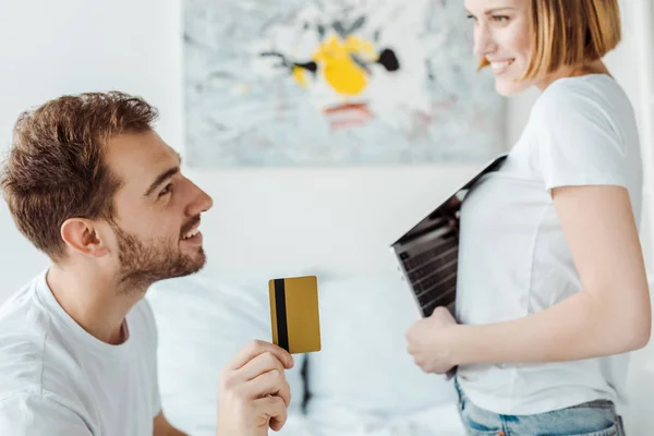 Casal sorrindo com laptop e cartão de crédito olhando um para o outro — Fotografia de Stock