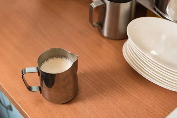 Stahlkrüge mit Milch und Tellern auf Holztisch — Stockfoto