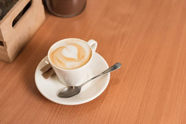 Taza de café con platillo y cuchara sobre mesa de madera - foto de stock