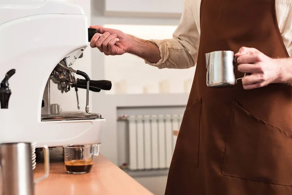 Обрезанный вид на баристу в коричневом фартуке, готовящего кофе — стоковое фото