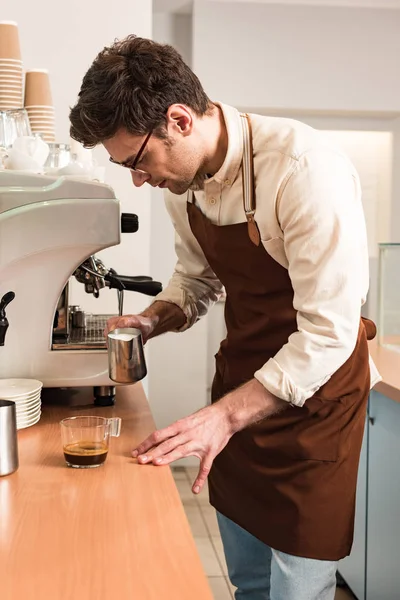 Бариста в очках и коричневом фартуке готовит кофе — стоковое фото