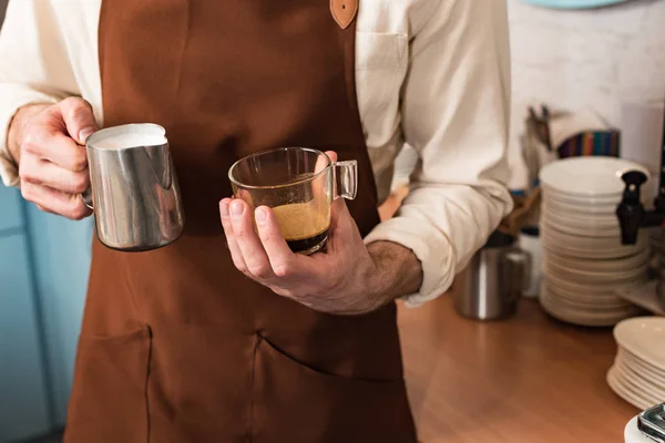 Partial view of barista holding cup of coffee and milk jug — Stock Photo