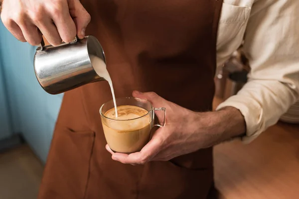 Обрезанный вид на баристу, наливающую молоко в кофе — стоковое фото