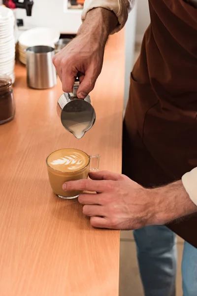 Cropped view of barista pouring milk in coffee — Stock Photo