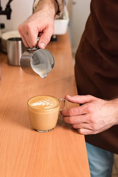 Cropped view of barista pouring milk in coffee — Stock Photo