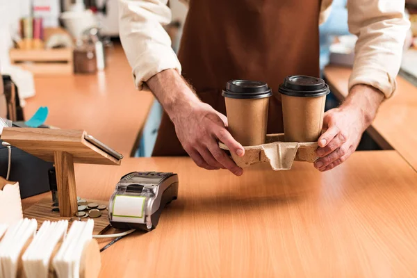 Vista cortada de barista em avental marrom segurando transportador copo take-out com café — Fotografia de Stock