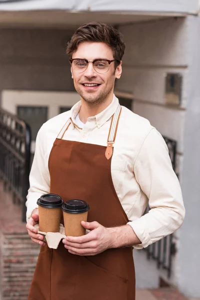 Smiling barista in glasses holding take-out cup carrier with coffee — Stock Photo