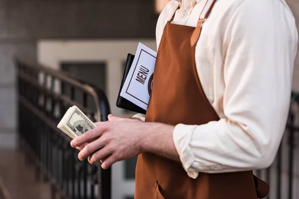 Vista parcial de barista en delantal celebración de menú y dinero en la calle - foto de stock