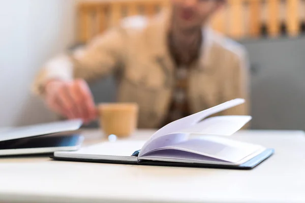 Selective focus of man with coffee and open notebook on table — Stock Photo