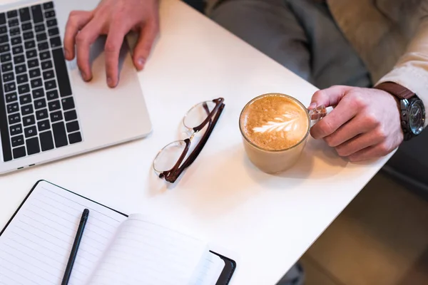 Cropped view of freelancer with cup of coffee and laptop in cafe — Stock Photo