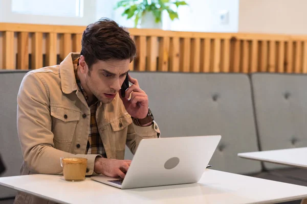 Freelancer ocupado falando no smartphone e usando laptop no café — Fotografia de Stock