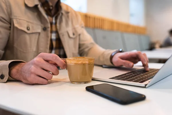 Vista recortada do freelancer com xícara de café digitando no teclado do laptop — Fotografia de Stock