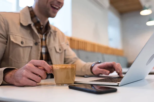 Cropped view of freelancer with cup of coffee typing on laptop keyboard — Stock Photo