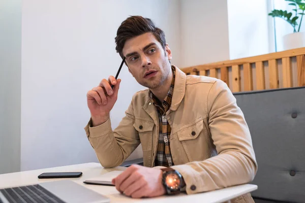 Pensive freelancer holding pencil while sitting at table in cafe — Stock Photo
