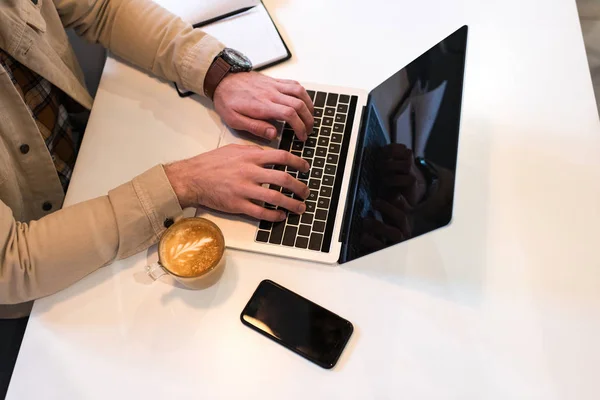 Vista parcial do freelancer com xícara de café digitando no teclado do laptop — Fotografia de Stock