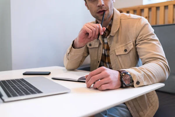 Cropped view of freelancer with laptop and notebook in cafe — Stock Photo