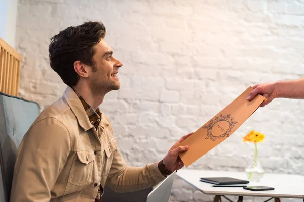 Laughing young man in jacket holding menu in cafe — Stock Photo