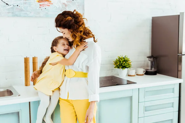 Mãe feliz rindo e abraçando com a filha juntos na cozinha — Fotografia de Stock