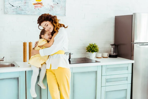 Felice madre abbracciando carina figlia in cucina — Foto stock