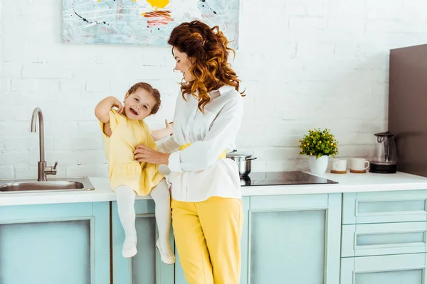 Beautiful mother looking at laughing daughter in kitchen — Stock Photo