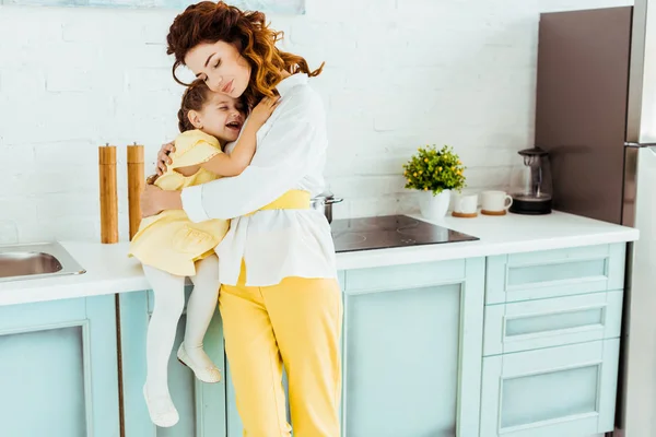 Mère heureuse embrassant fille excitée dans la cuisine — Photo de stock