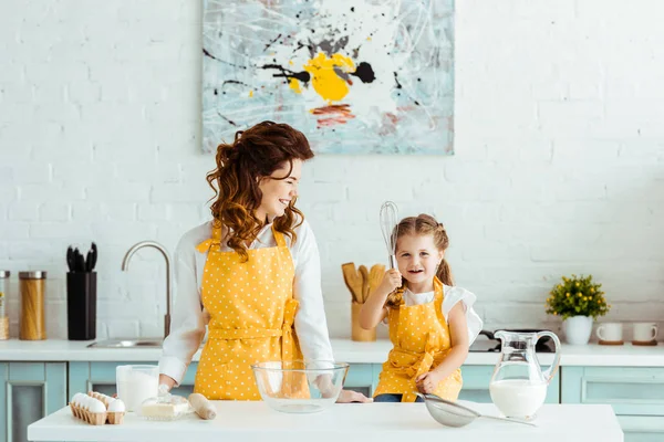 Happy mother and daughter in polka dot yellow aprons cooking together in kitchen — Stock Photo