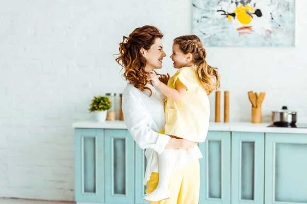 Happy mother holding smiling daughter in kitchen — Stock Photo