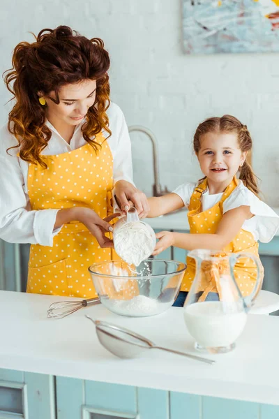 Mère aidant fille heureuse ajoutant de la farine au bol dans la cuisine — Photo de stock