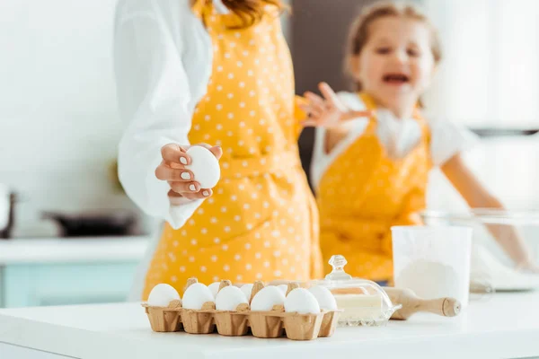 Foyer sélectif de gamin étirant la main à l'oeuf près de la table avec des ingrédients de boulangerie — Photo de stock