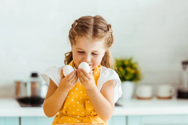 Cute kid in yellow polka dot apron looking at eggs in kitchen — Stock Photo