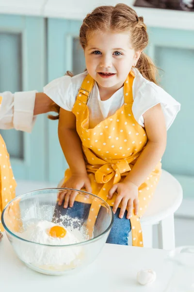 Mother touching daughter in apron near bowl with flour and smashed egg — Stock Photo