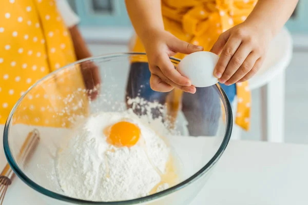 Vista recortada del niño añadiendo huevos a la harina en un tazón de vidrio - foto de stock