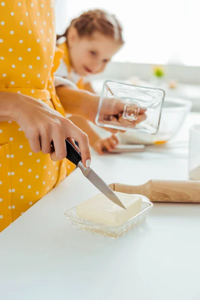 Enfoque selectivo de la mujer cortar mantequilla con cuchillo cerca de la hija - foto de stock