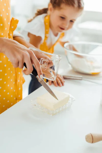 Selective focus of mother cutting butter with knife near daughter — Stock Photo