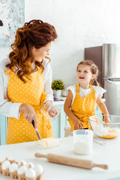 Селективное внимание женщины режет масло и смотрит на счастливую дочь на кухне — стоковое фото